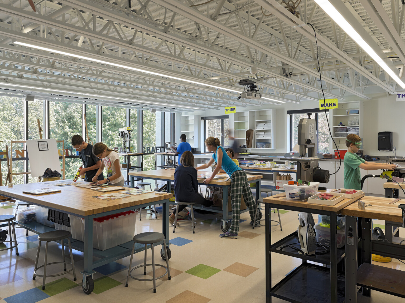 students collaborate in well-lit open-concept learning environment, floor-ceiling windows, natural lighting illuminate light wood desks and work tables