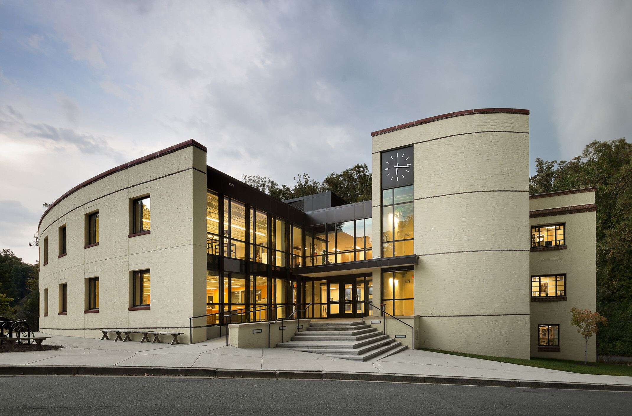 Three-story building, concrete, tile and steel, interior floor-to-ceiling windows, cloudy skies at dusk