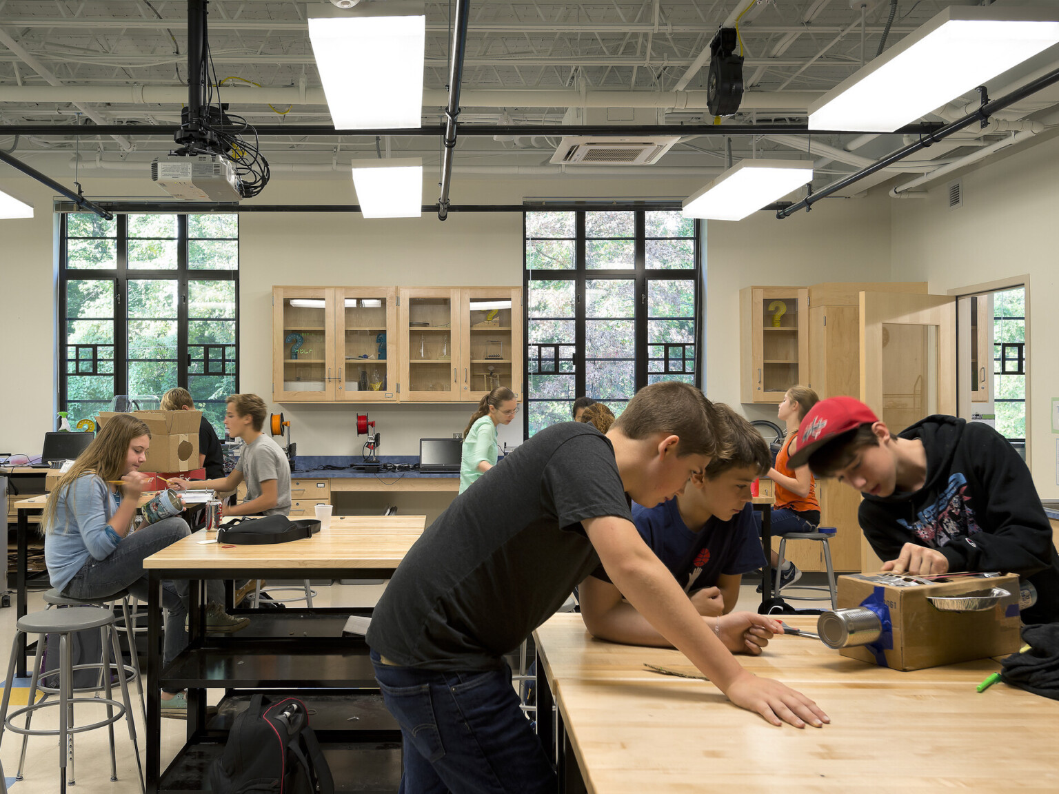 students collaborate in well-lit open-concept learning environment, floor-ceiling windows, natural lighting and natural light wood desks and work tables