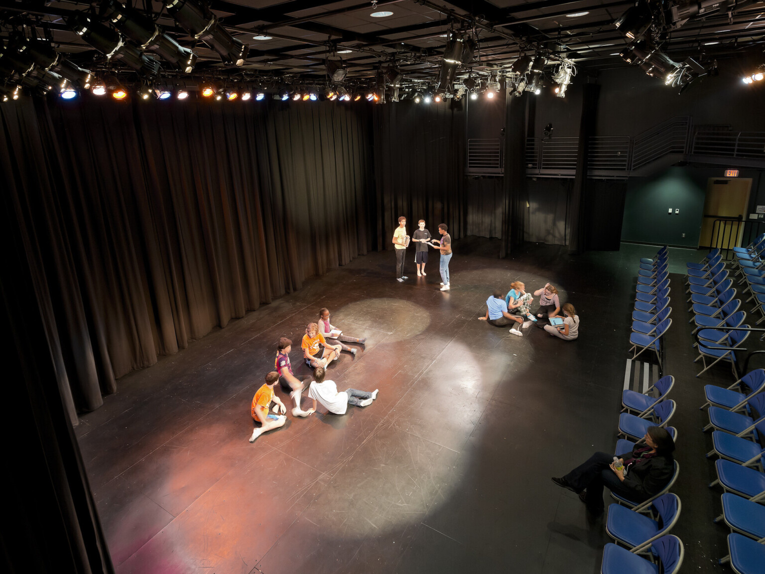 Stage for student's performance with actors, spotlights, rigging gear, audience seating