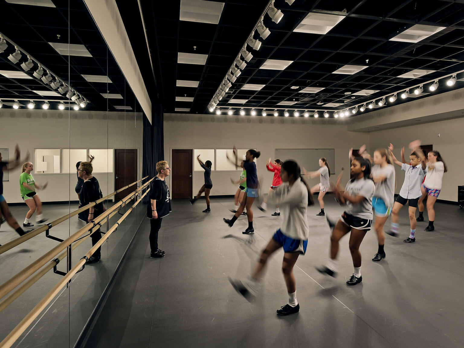students learn dance moves in front of full-length mirrors, with balance bar, custom overhead lighting and flooring