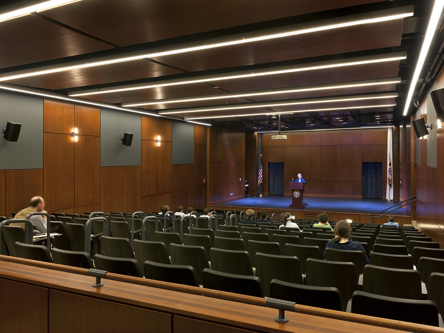 theater with black seating, acoustic panel ceiling, custom overhead lighting and sound system, wooden stage with podium