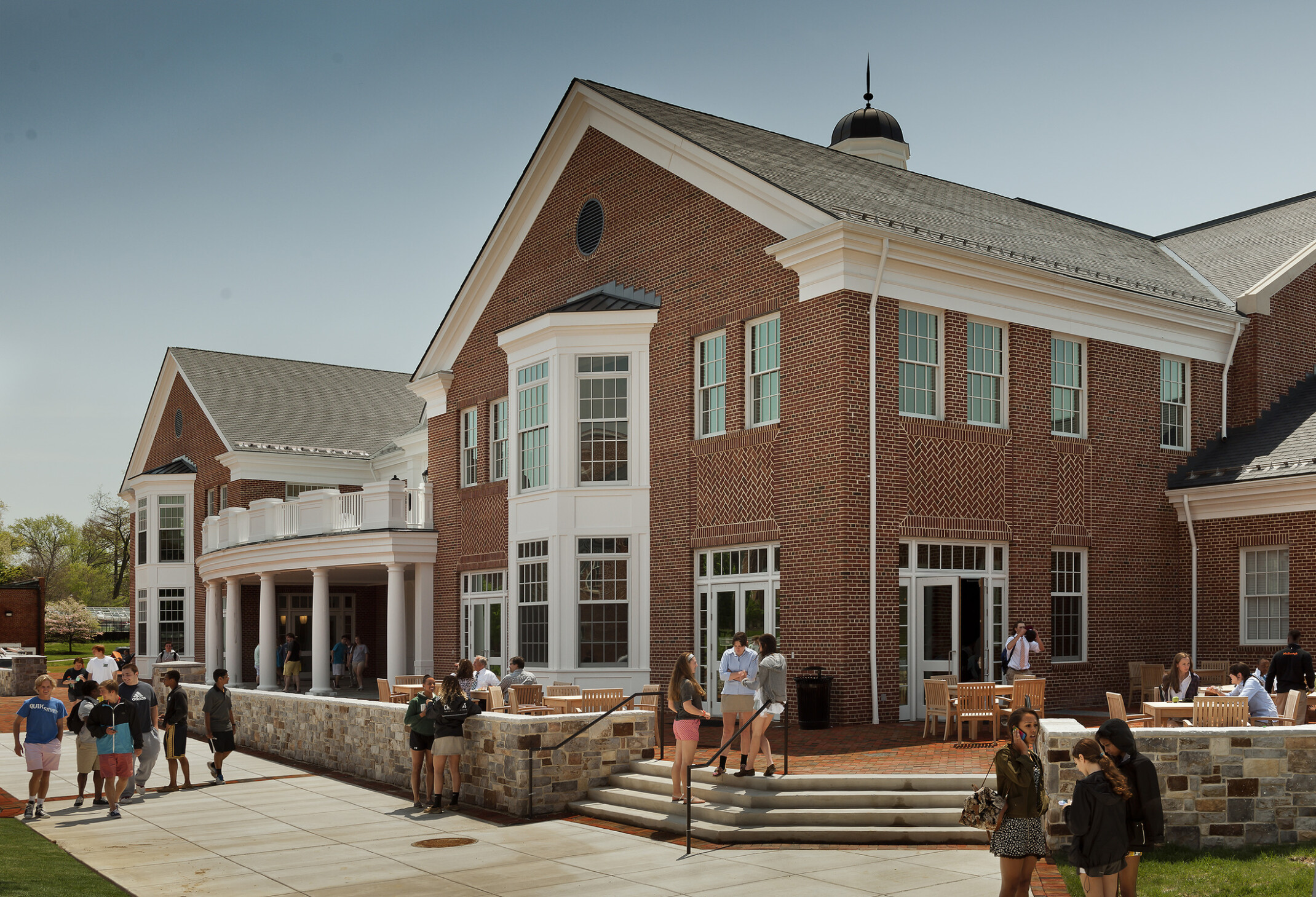 Red brick three-story Georgian-style facade, bay windows, concrete steps and walkway to entrance, large copper cupola, chimneys, gray stone base