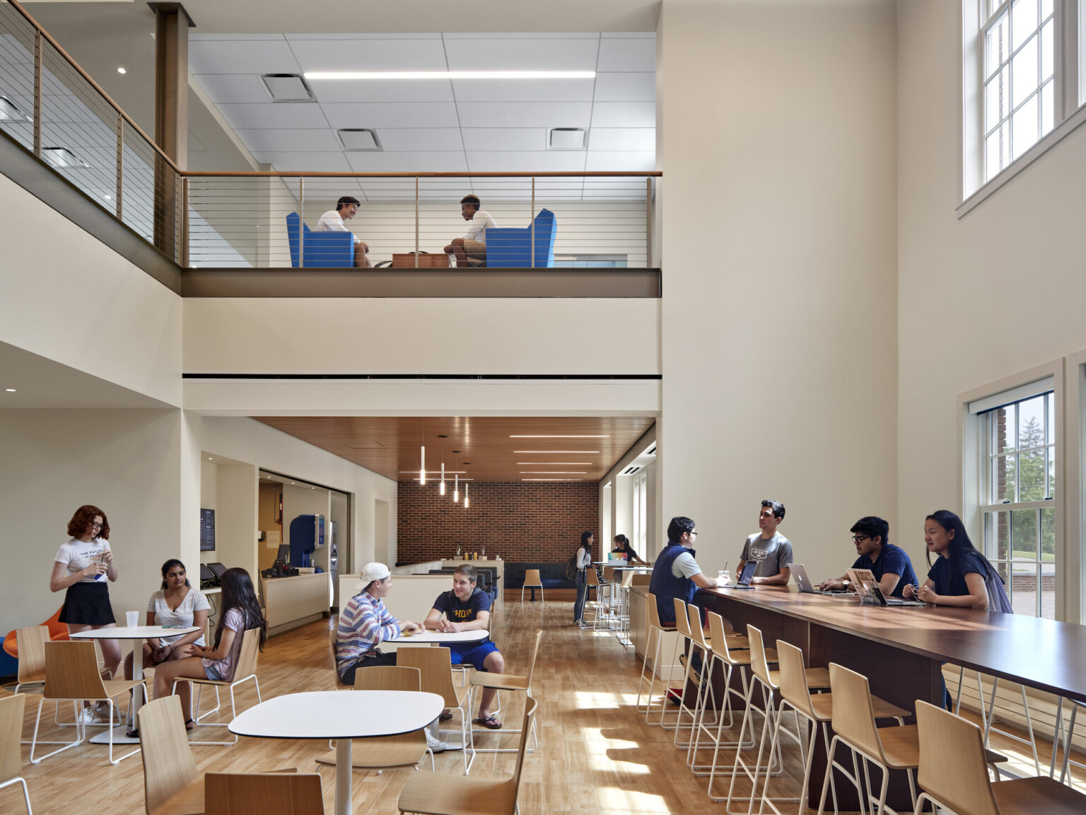 Double height dining hall cafe space with tables, chairs, bar height counter, booths, view to second floor balcony seating