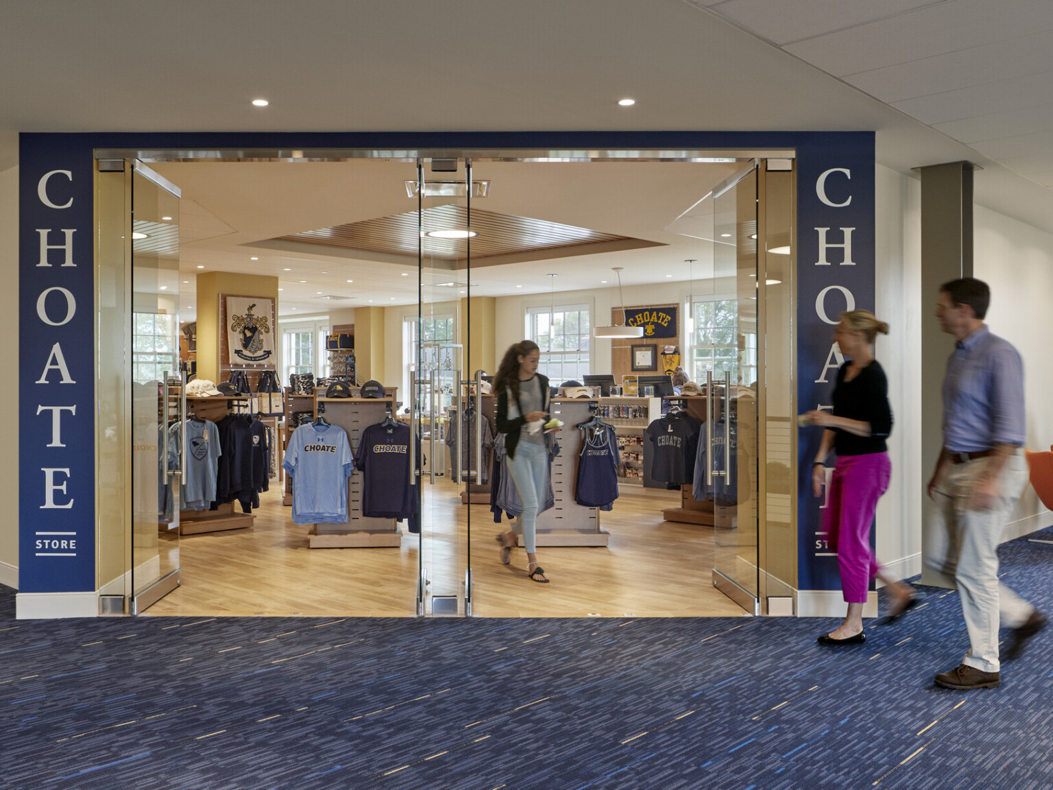 Choate student store with blue school branding with wood flooring off blue carpeted hall, large windows in both spaces