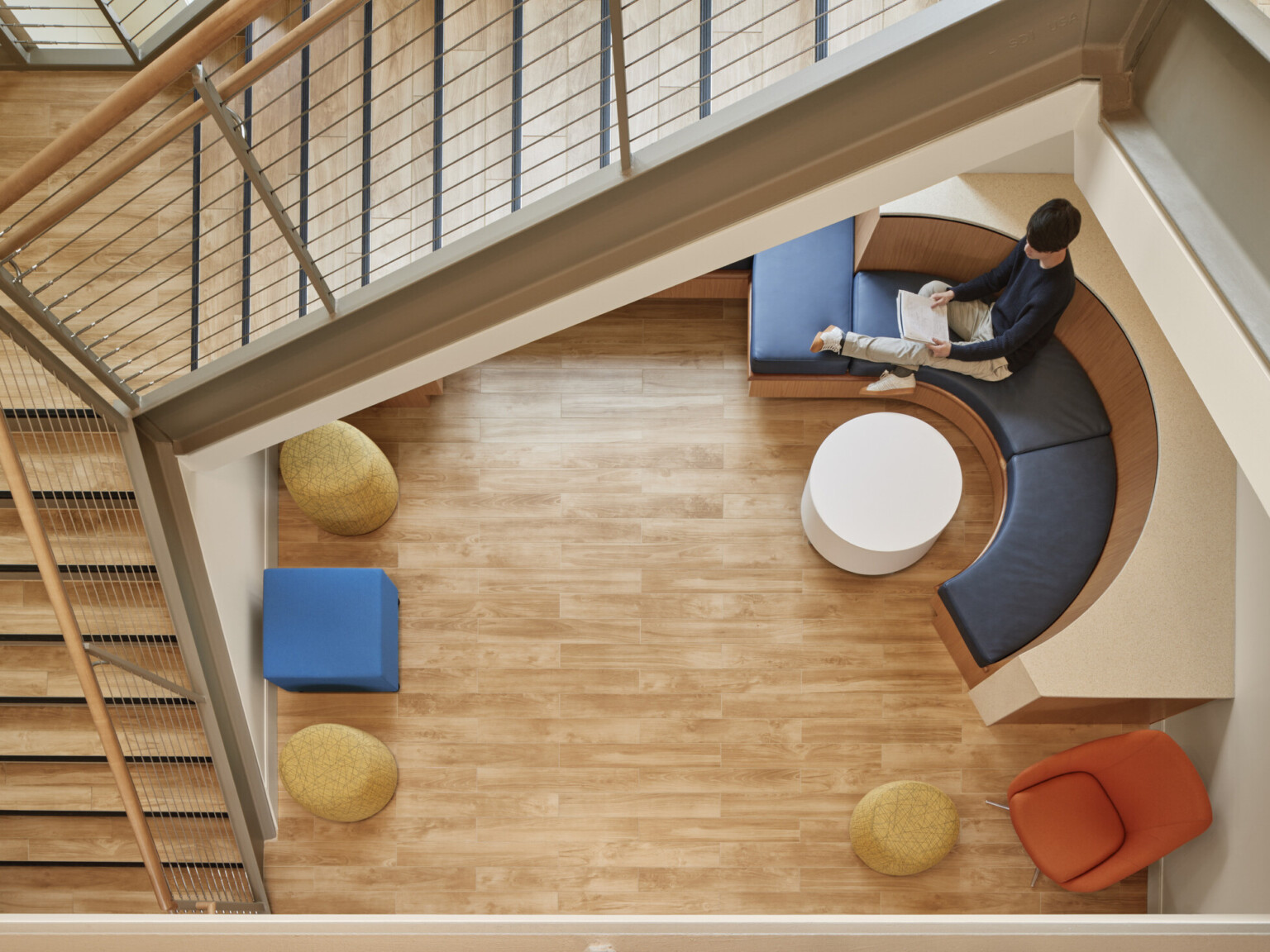 Top of wood stairwell looking to mixed comfortable seating at lower level, rounded bench seat next to window lit with natural light