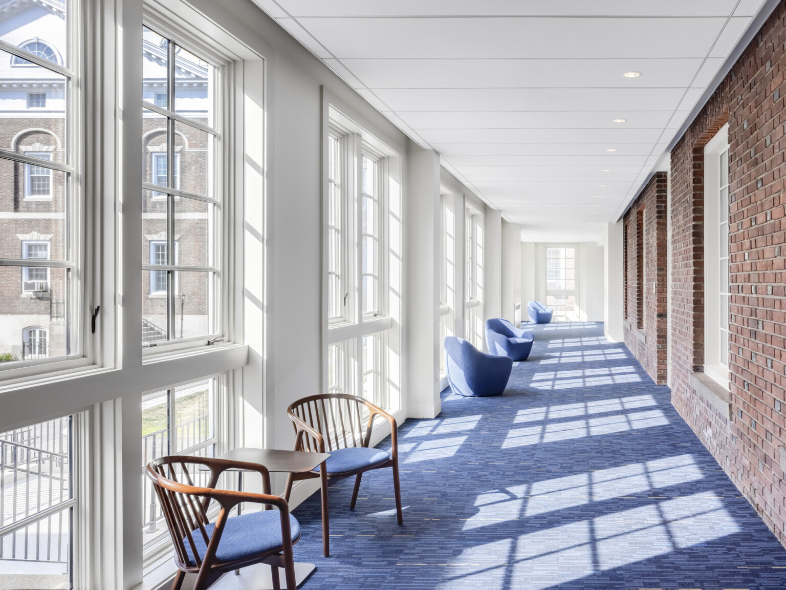 Four season room addition with exposed brick, carpet, mixed seating along floor to ceiling double sash windows looking to courtyard