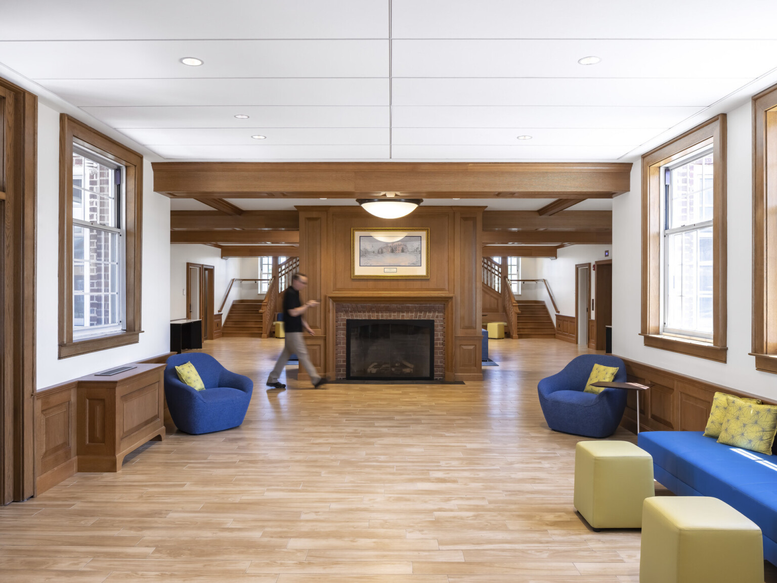 Interior common space lined with windows, mixed comfortable seating, central brick fireplace in front of grand double staircase