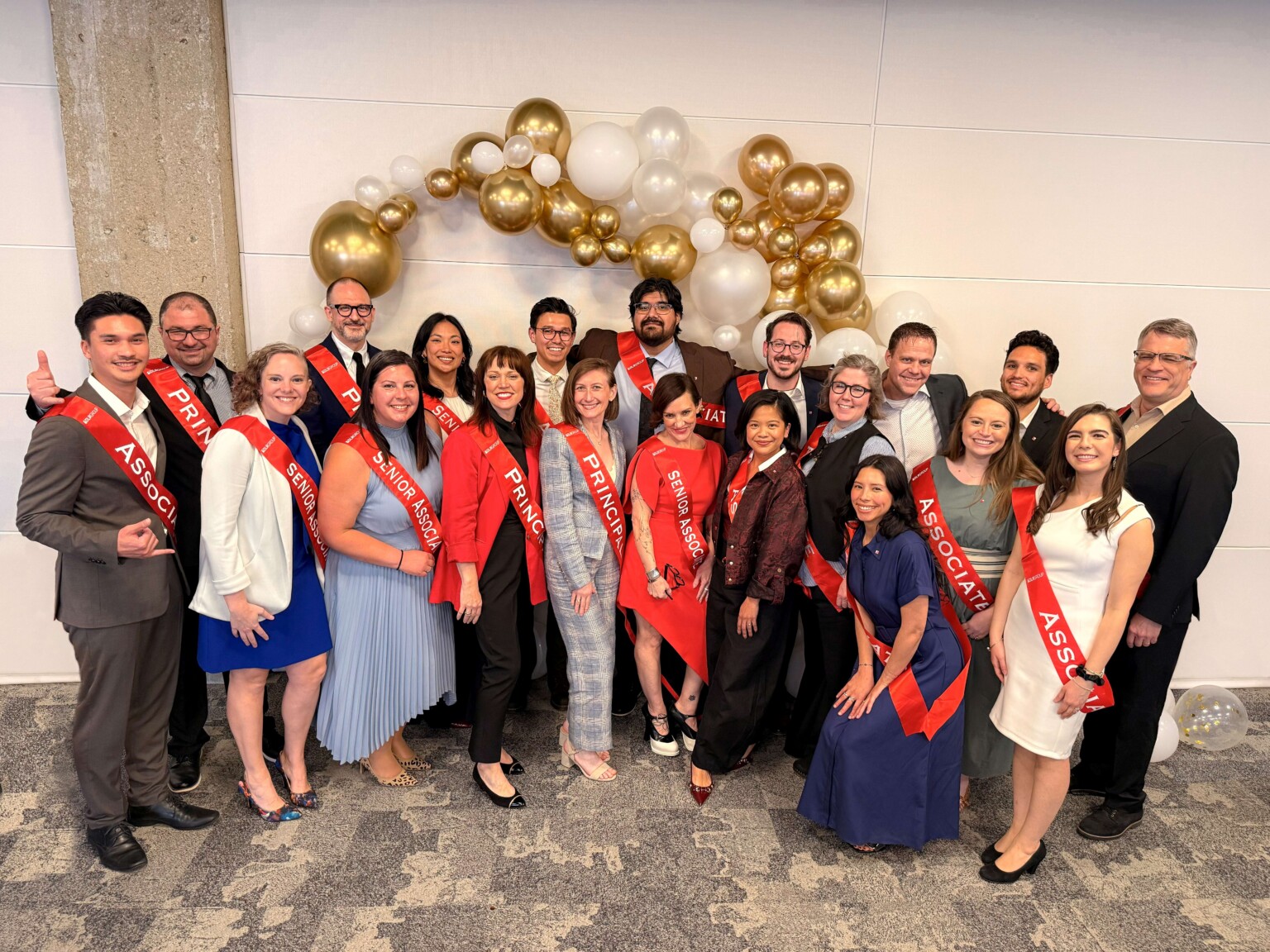 DLR Group employees stand in front of balloon arch with with appointment level red sashes on