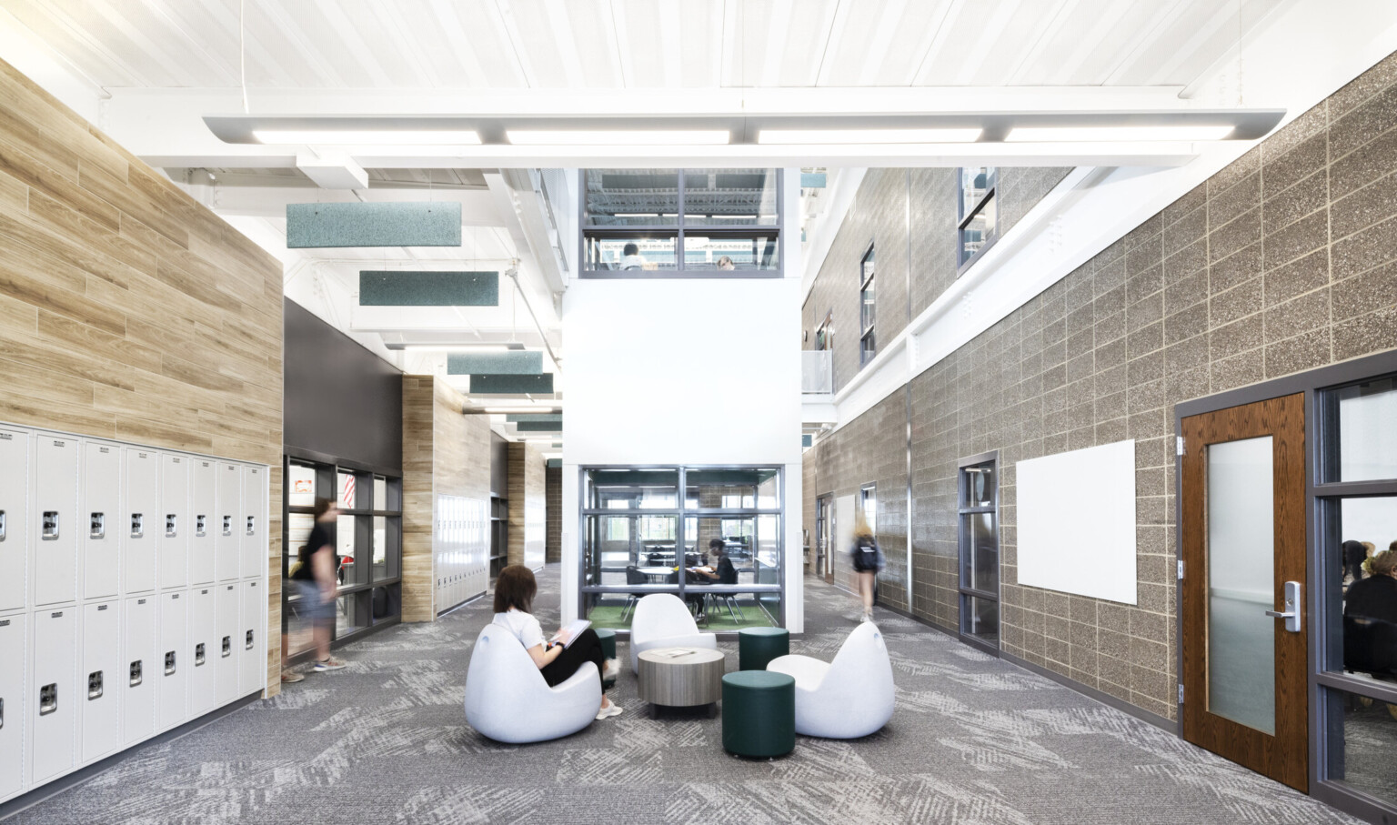 image of a collaboration space in a school with lockers; breakout lounges for student interaction; modular furniture; lockers on the wall in double height hallway
