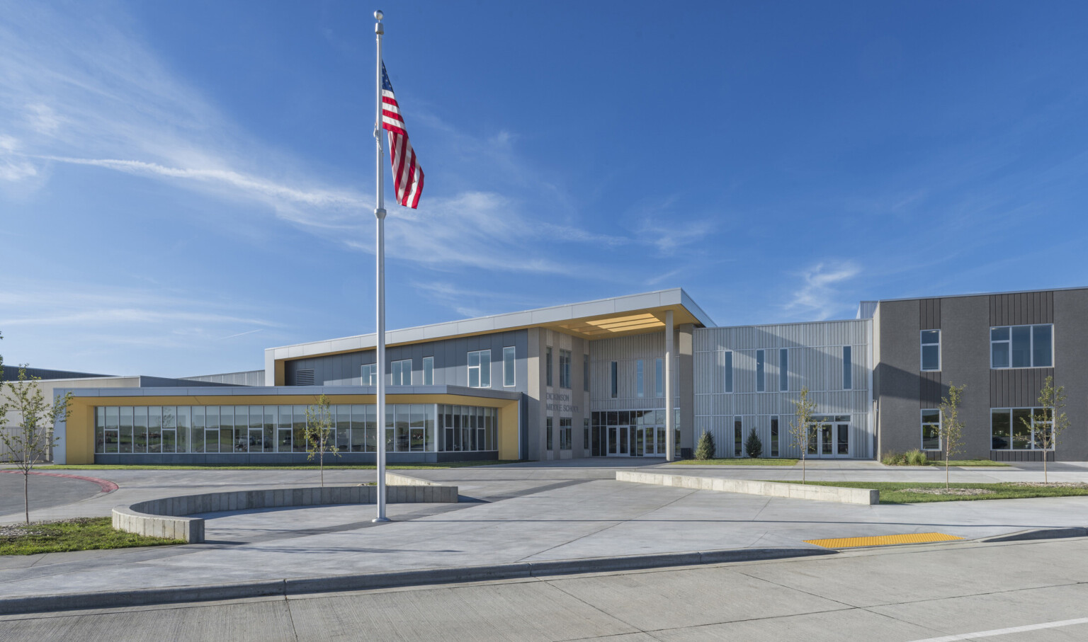 Exterior of 2 story grey panel building with silver wrapped facade and yellow under side of overhangs and canopy. Flag, front