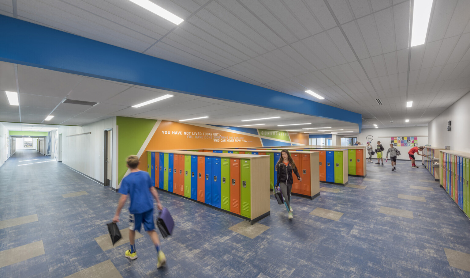 Hall height multicolor lockers in rows and along wall of room with brightly colored geometric mural with quote on left wall