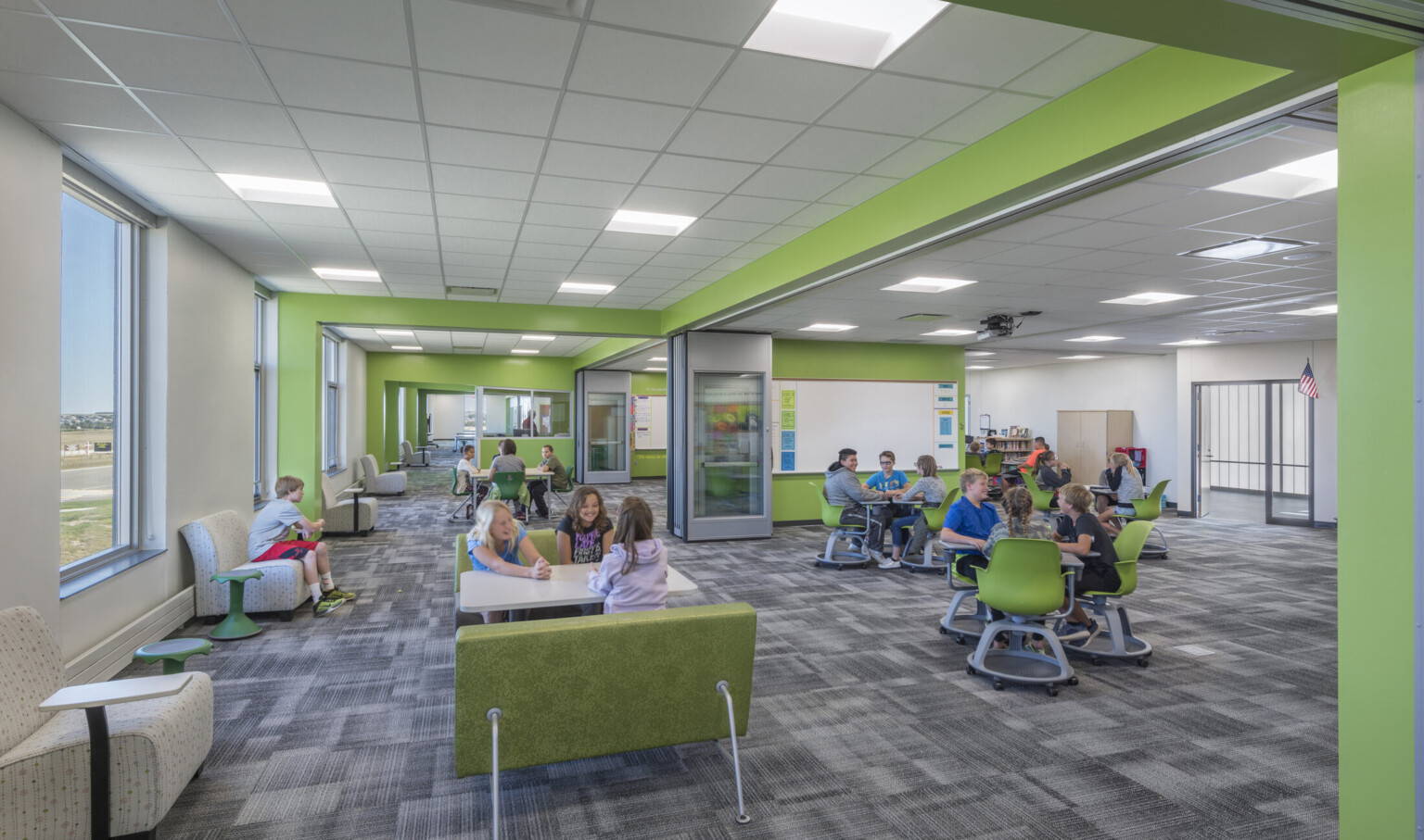 Large white room with green accents and flexible seating. Flexible interior walls create smaller spaces. Windows, left