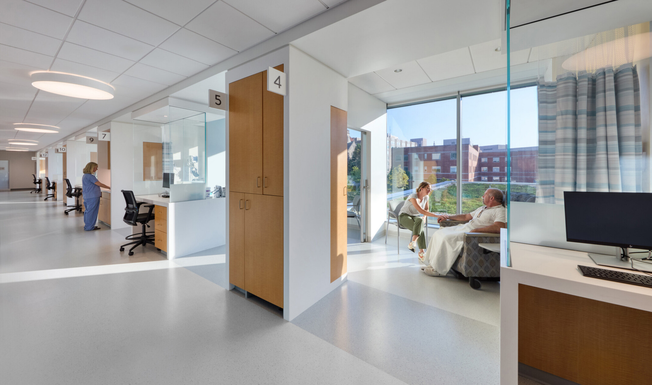 Physician and patient area in the OSF Cancer Institute and Proton Therapy building; bright natural light behind the patients and doctors in the space; modern white with light wood details on the cabinets; computer stations throughout