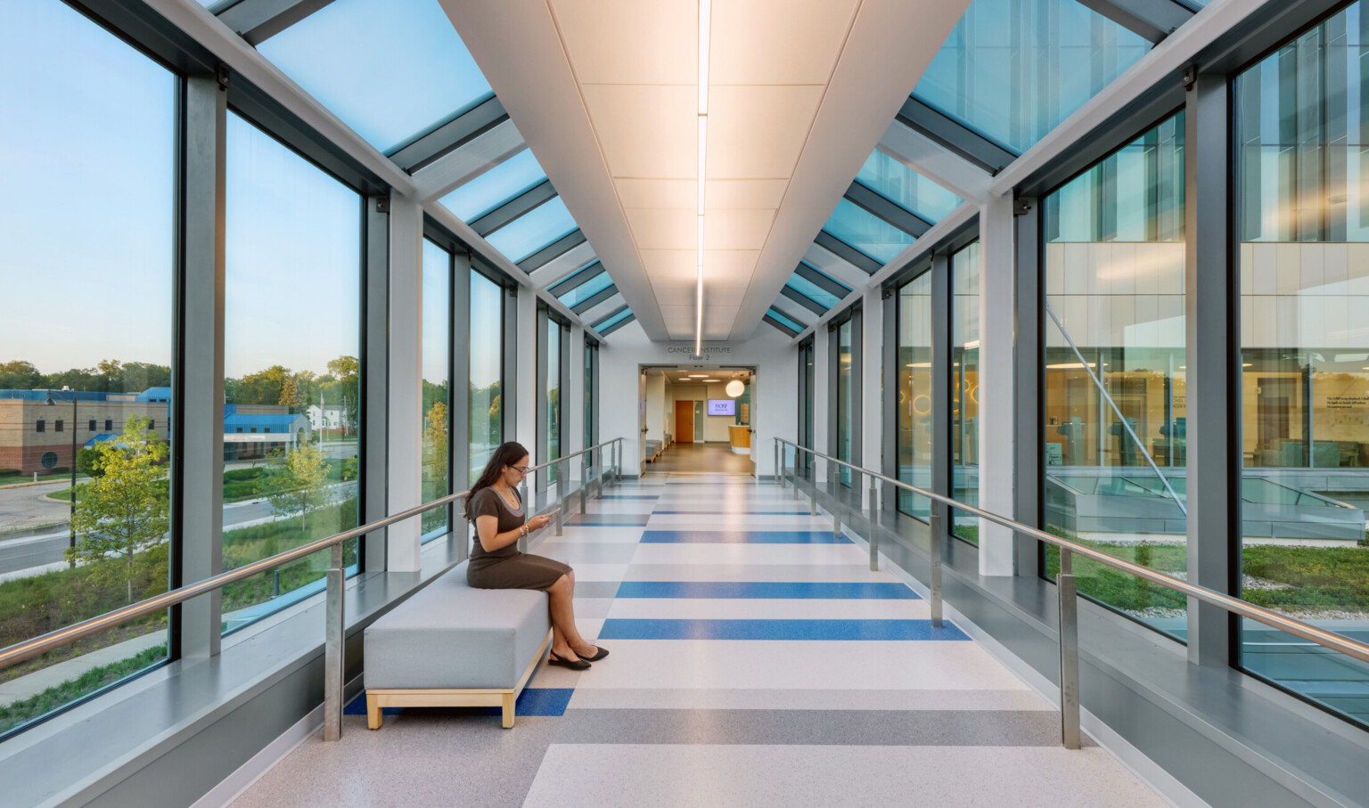 Symmetrical, brightly naturally lit hallway with one women sitting on a bench to the left