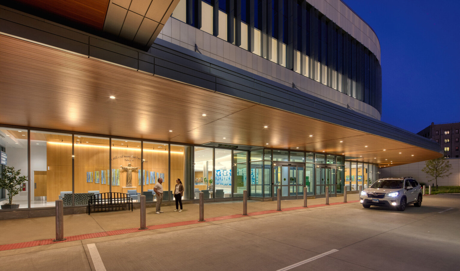 Nighttime view of OSF Cancer Institute and Proton Therapy building; vehicle and pedestrian entrance highlighted with lighting inside showcasing healthcare design in the waiting area