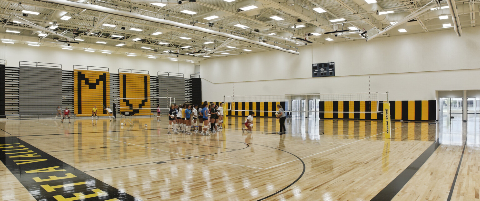 basketball court gynmasium, translucent wall panels filter natural light into the school’s common spaces, shhiny wood floors painted with school colors, team name. overhead lighting