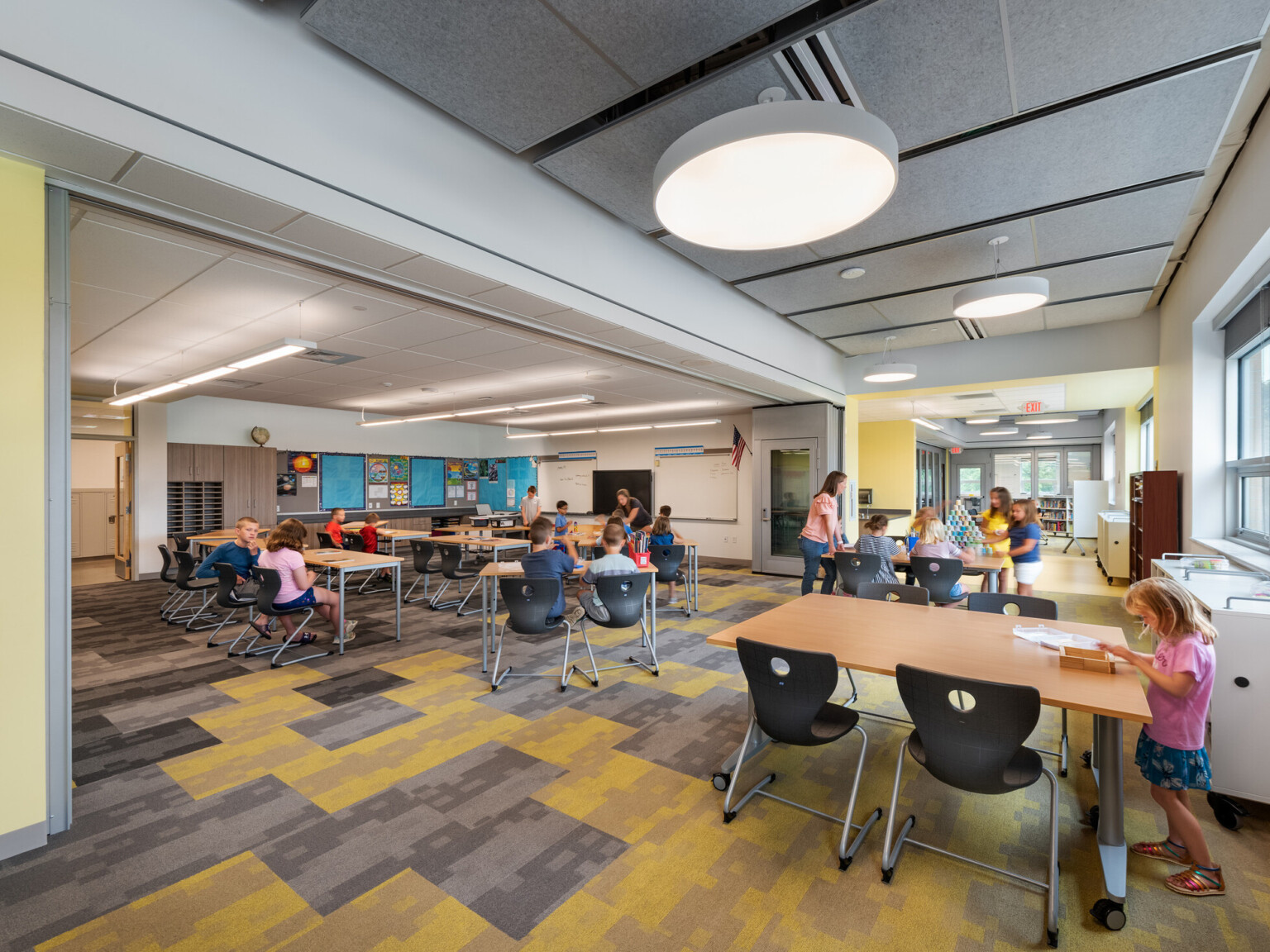 Flexible wall opened in the middle of large classroom, pastel yellow paint, yellow and grey rug, flexible workspaces