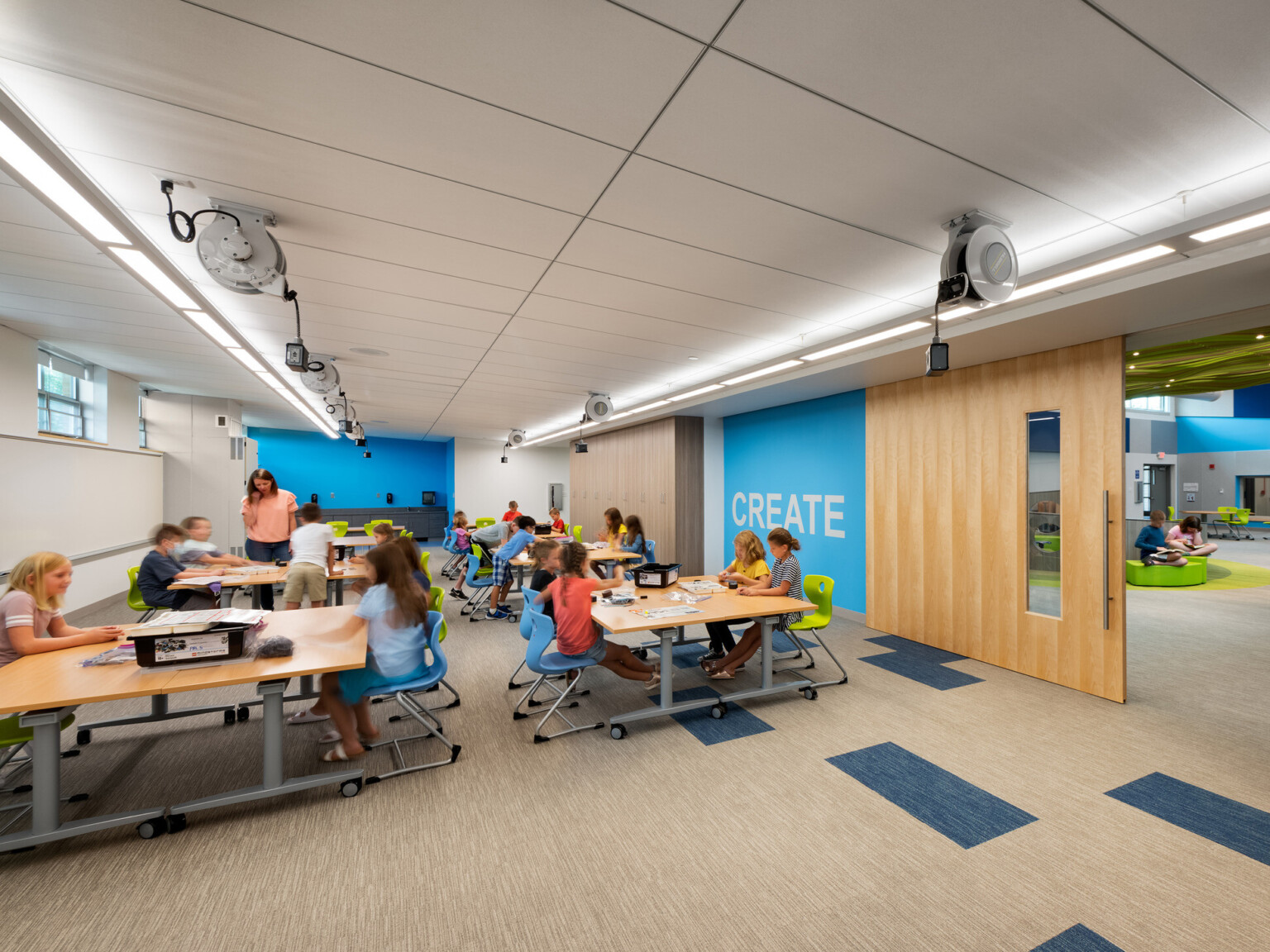 Long classroom with wood sliding door to open space, blue accent way with mural reading create