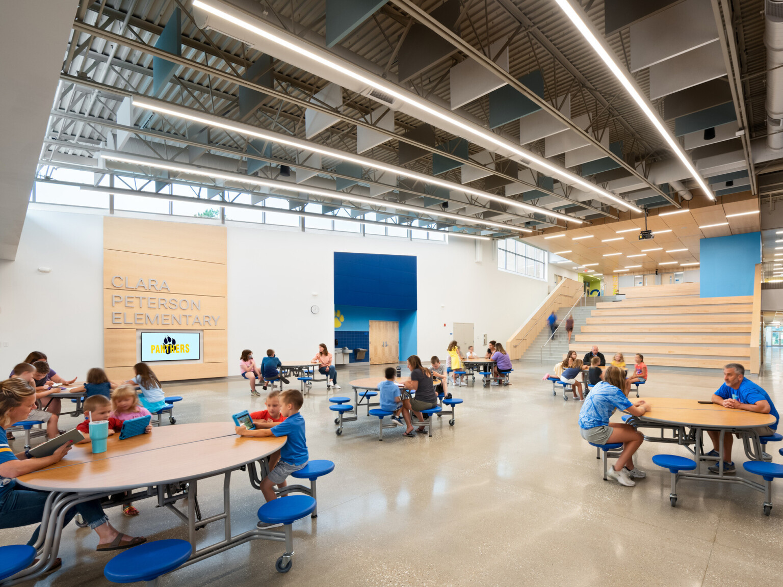 Double height cafeteria common space with flexible seating and tables, learning stairs to second floor
