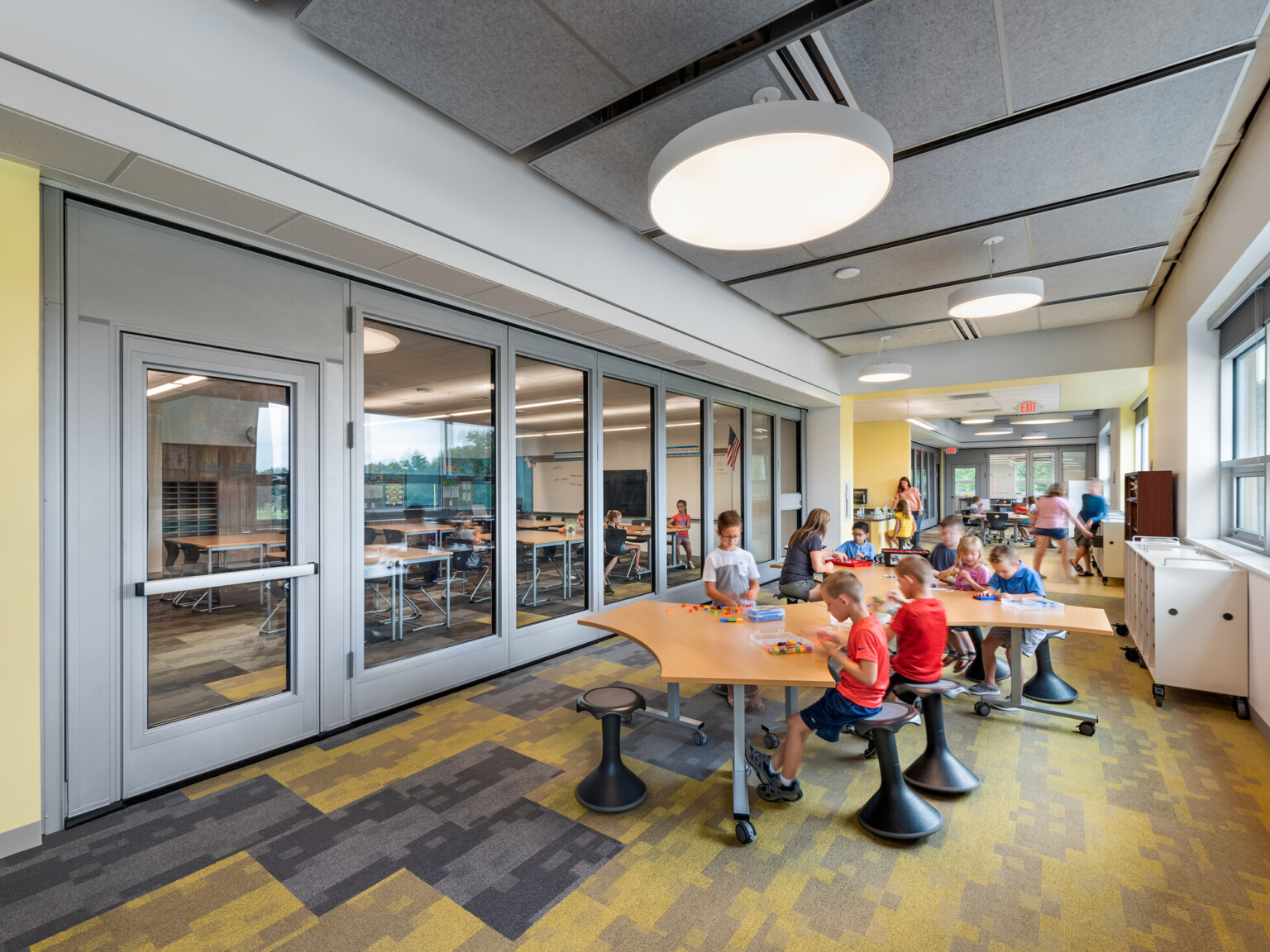 Same space with glass wall pulled closed creating two smaller classrooms, furniture arranged with long table