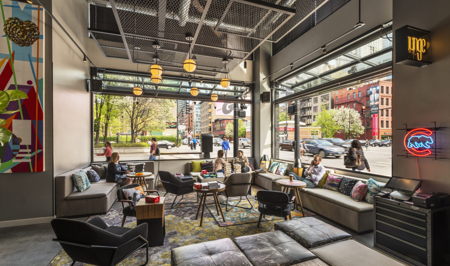 Interior corner with flexible and comfortable seating. Windows on both walls opened. Geometric metal pendant lights hang