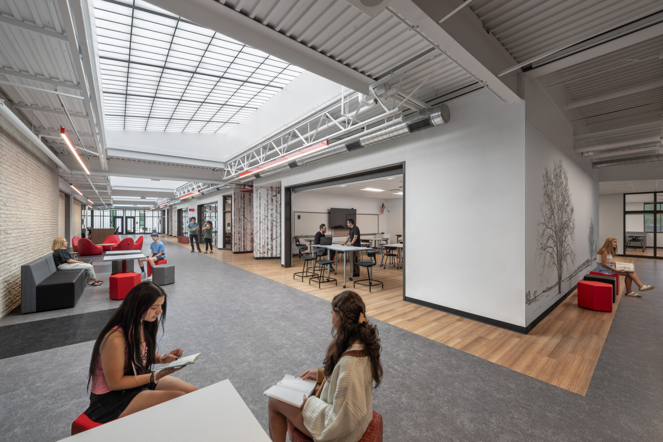 Students sitting on red chairs in a collaborative space with grey walls and flooring with wooden accents.