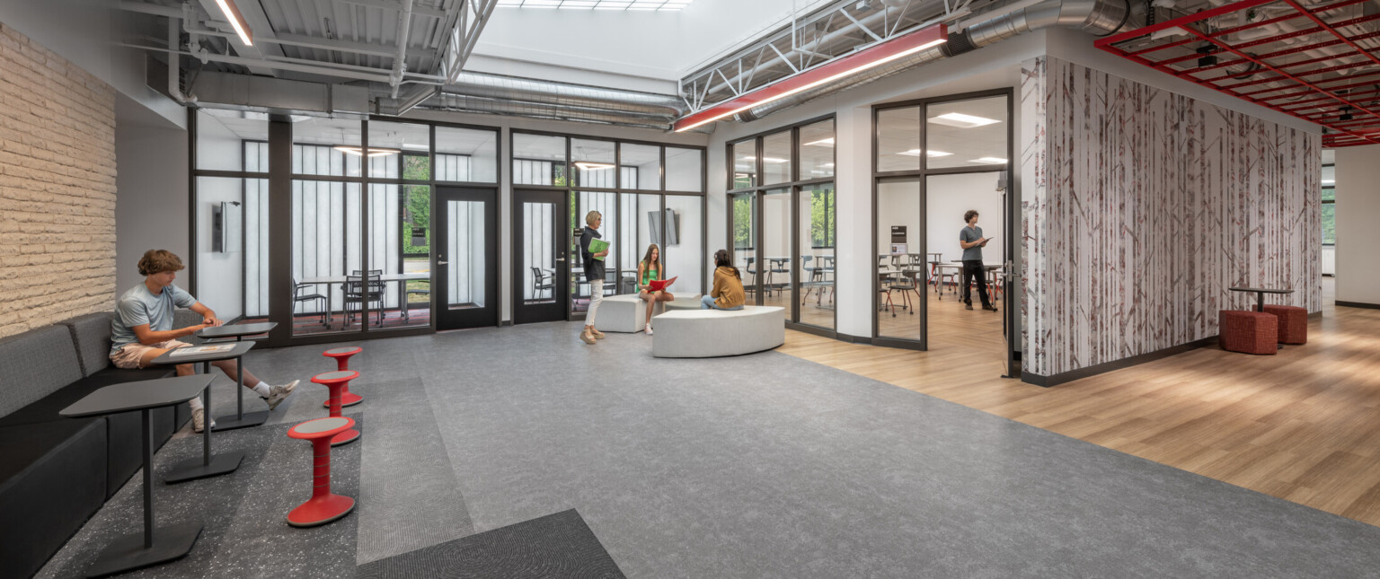 Collaborative learning space with grey and wood floors, black framed windows, and red furnishing
