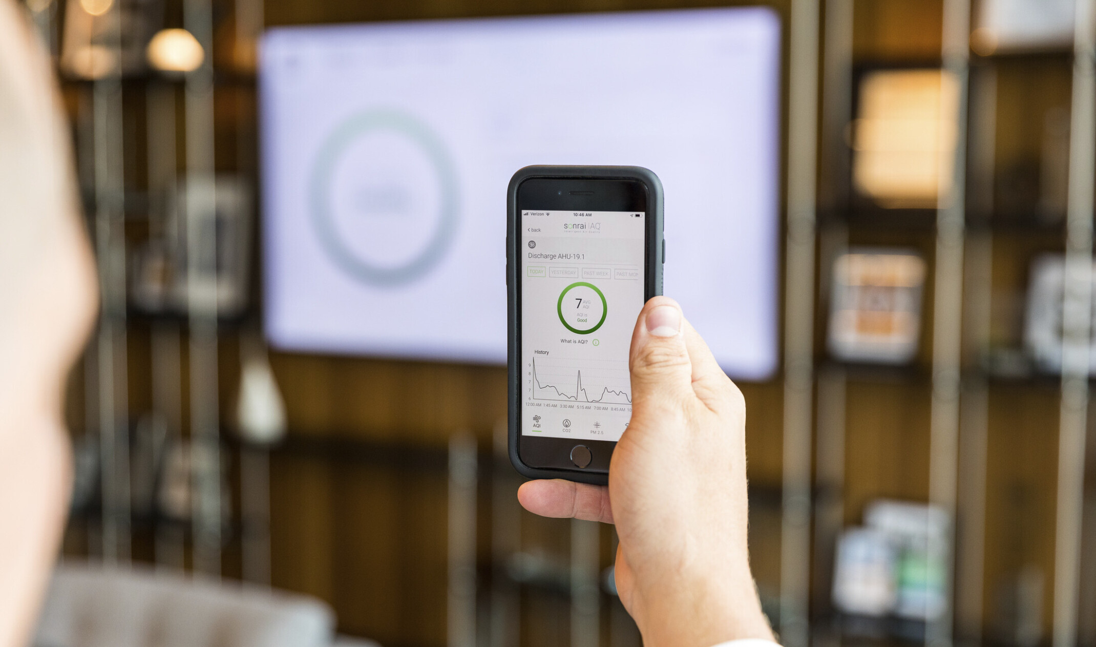 person using sonrai IAQ app in a space to read live air quality metrics, which are also shown on the lobby screen in front