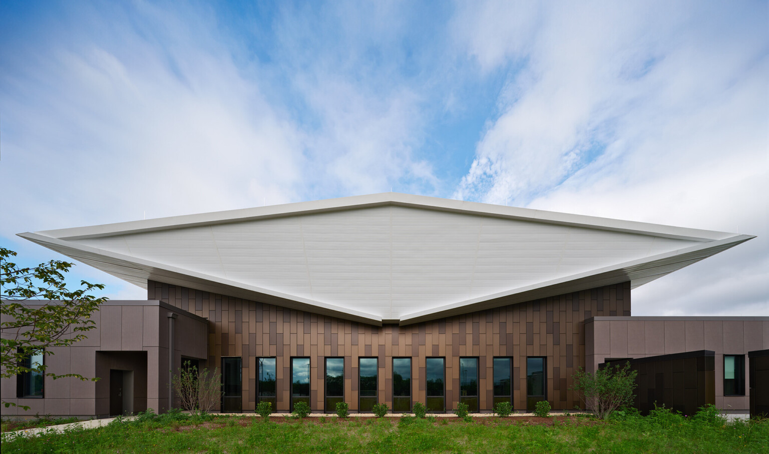 Exterior of lake county regional operations and communications facility; Head-on view of the building’s exterior end shows the white double-butterfly roof as a diamond-shaped volume that floats above the dark brown textured building exterior that is pieced by narrow vertical windows.