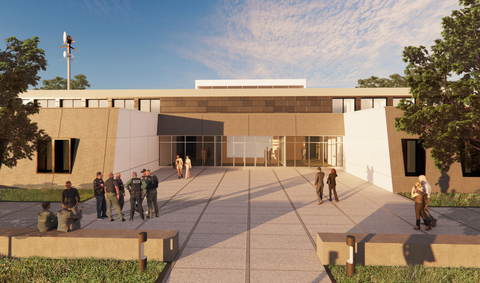 Rendering of entrance to Lake County Regional Operations & Communications Facility; one-story brick building with white butterfly wing roof and tall communications antenna on a grassy site with wide sidewalks around the perimeter and a main drive that is protected by bollards at the entrance; emergency professionals sit and walk outside the entrance