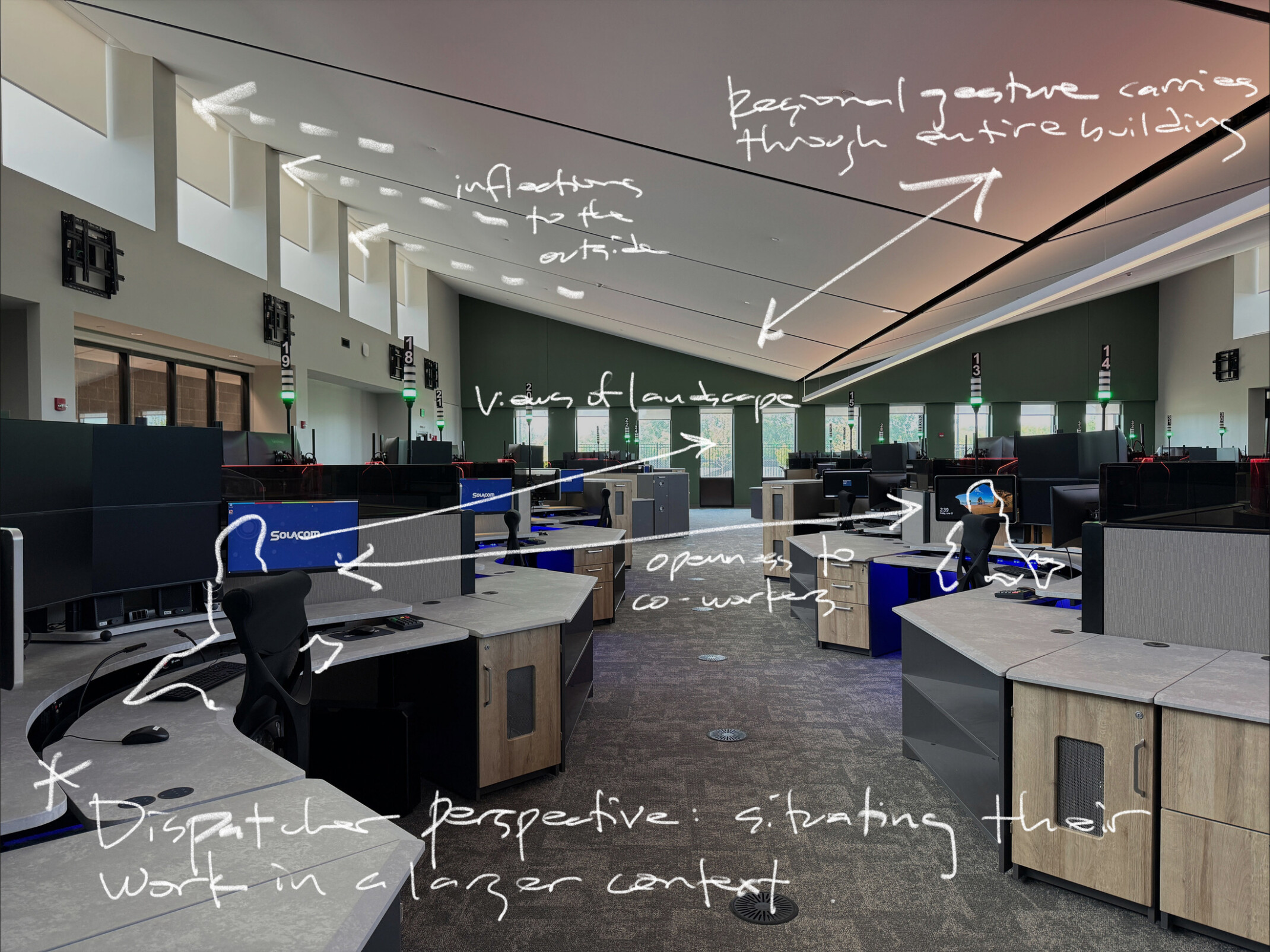 Indoor image featuring an open bullpen office space with several desk stations, computer monitors, and natural daylight from high windows; overlaid handwritten notes from architect