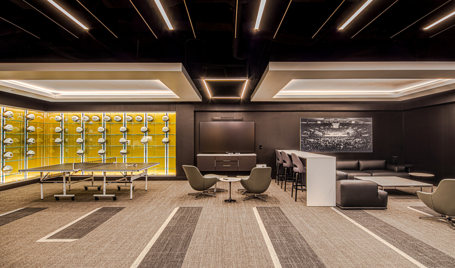 Lounge area featuring glass cases filled will basketballs with a yellow wall, multiple seating areas divided by a bar height table and chairs
