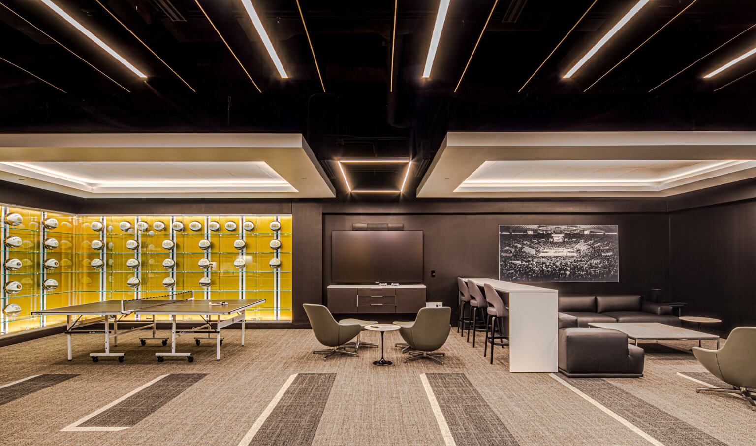 Lounge area featuring glass cases filled will basketballs with a yellow wall, multiple seating areas divided by a bar height table and chairs