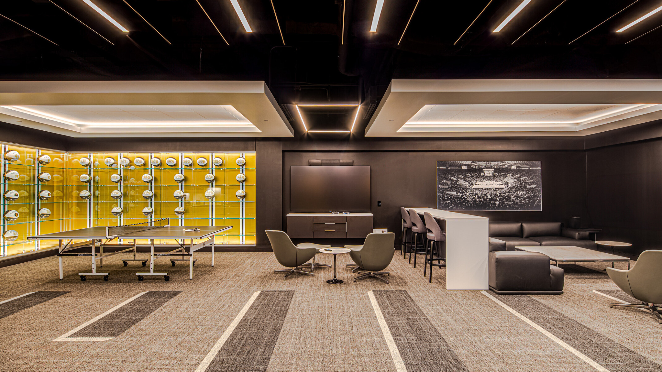 Lounge area featuring glass cases filled will basketballs with a yellow wall, multiple seating areas divided by a bar height table and chairs