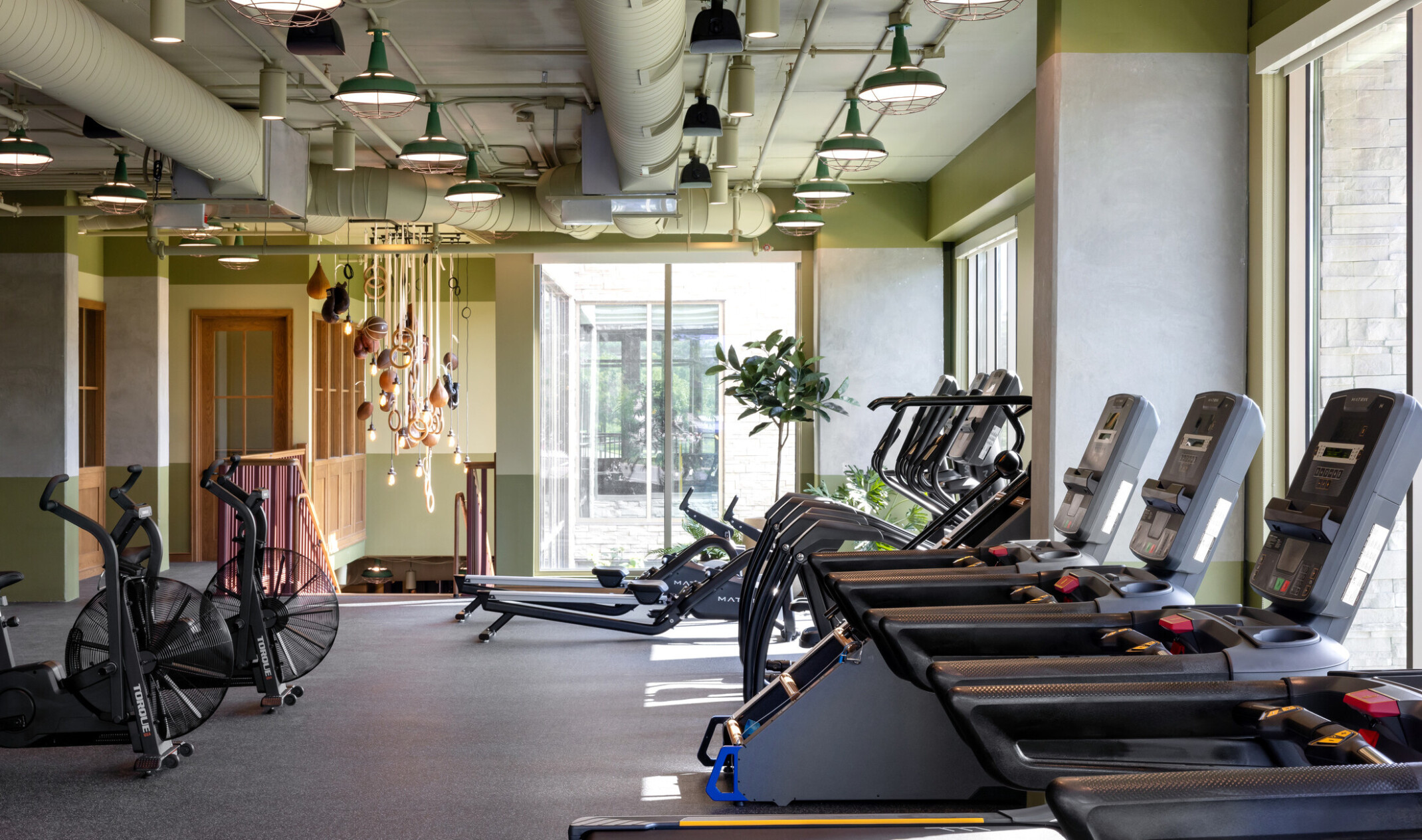 Hub Bloomington off campus student housing; Industrial-style fitness center with exposed concrete, green accents, and workout equipment.