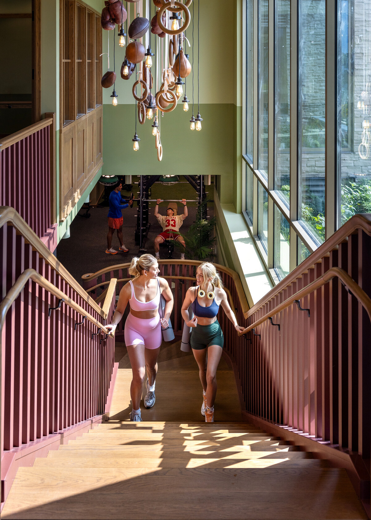 Hub Bloomington off campus student housing; Students walking up wood stairs beneath a sculptural sports-inspired light installation.