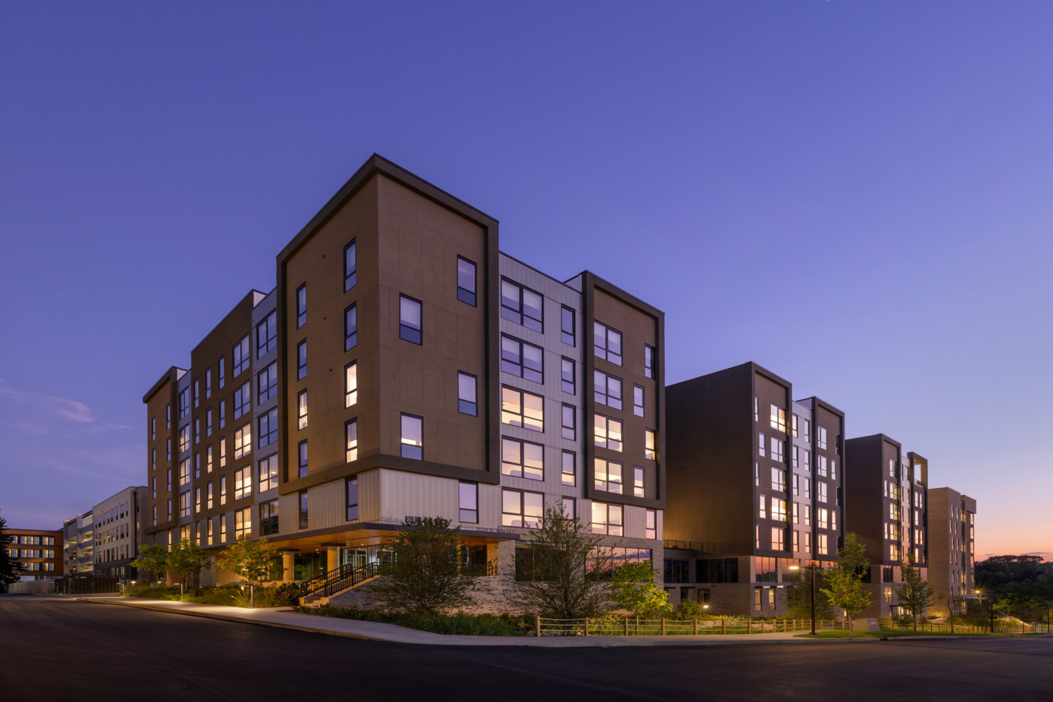 Hub Bloomington off campus student housing; Primary building entrance at dawn with layered exterior materials and landscaped stormwater edge