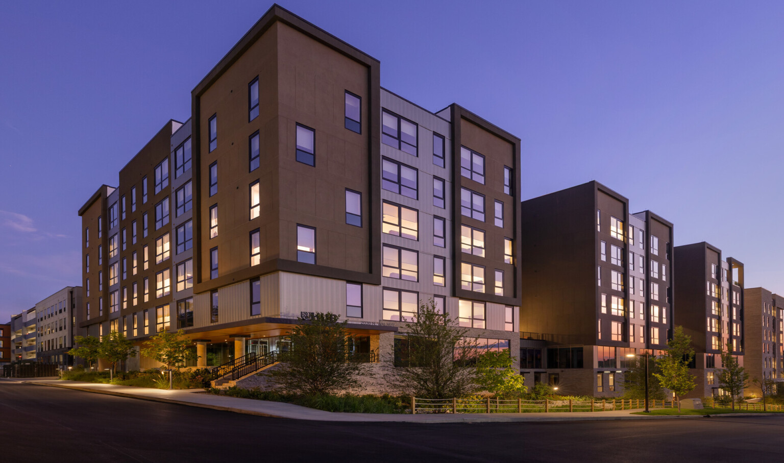 Hub Bloomington off campus student housing; Primary building entrance at dawn with layered exterior materials and landscaped stormwater edge