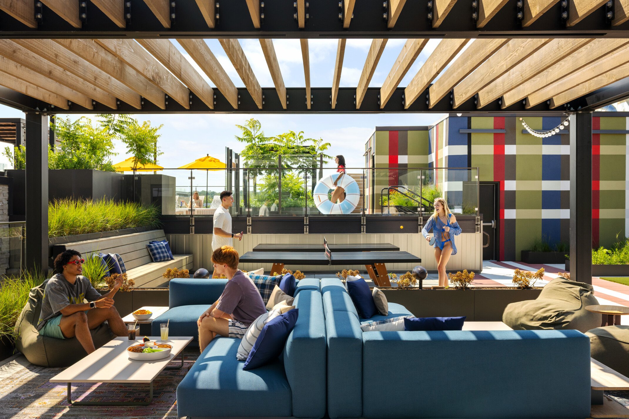 Hub Bloomington off campus student housing; Outdoor rooftop lounge featuring blue furniture, shaded seating, ping pong tables, and a large-scale plaid mural