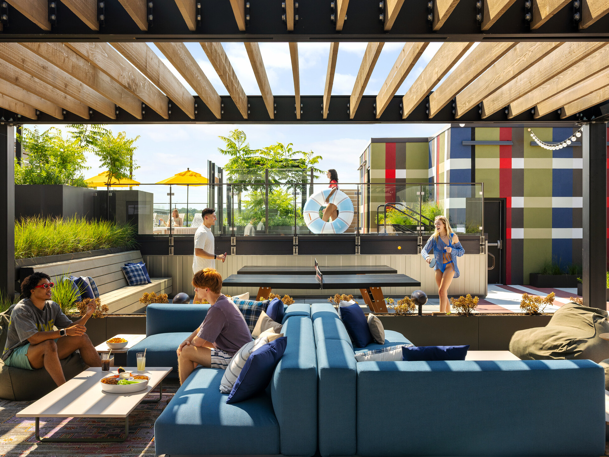 Hub Bloomington off campus student housing; Outdoor rooftop lounge featuring blue furniture, shaded seating, ping pong tables, and a large-scale plaid mural