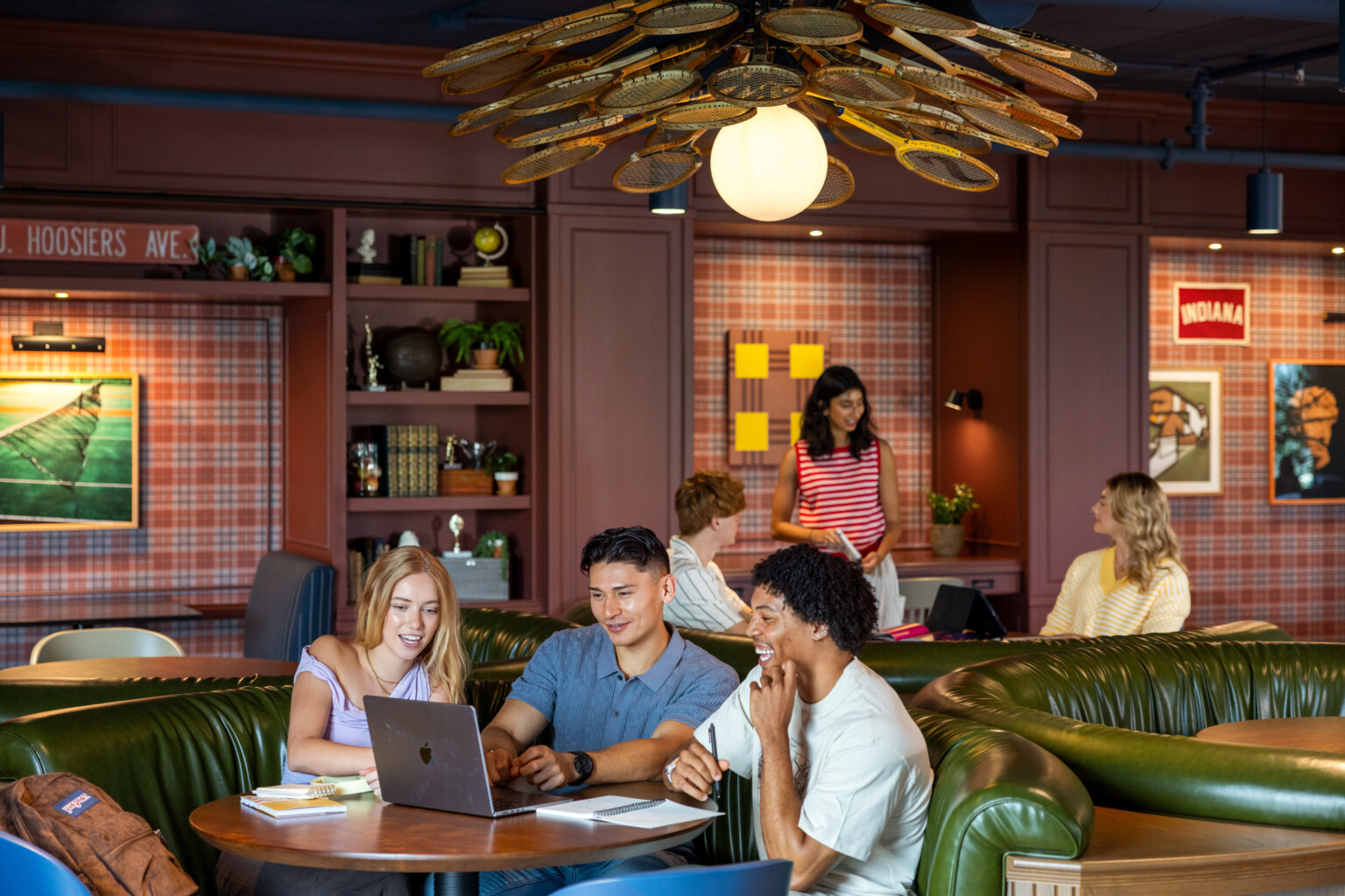 Hub Bloomington off campus student housing; Students studying and talking in booth seating under a badminton-racket light fixture.