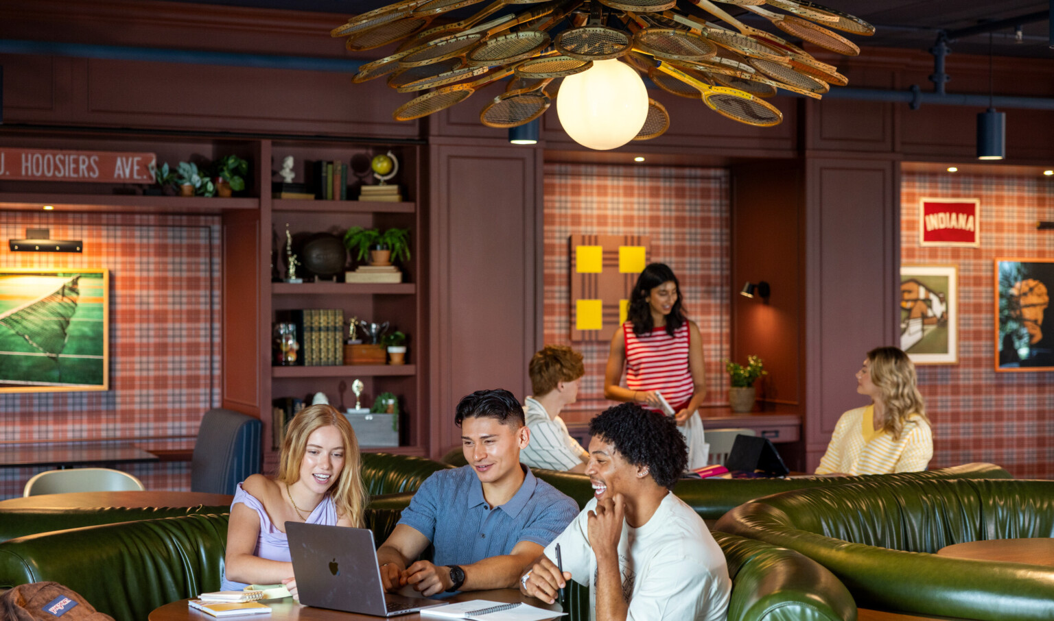 Hub Bloomington off campus student housing; Students studying and talking in booth seating under a badminton-racket light fixture.