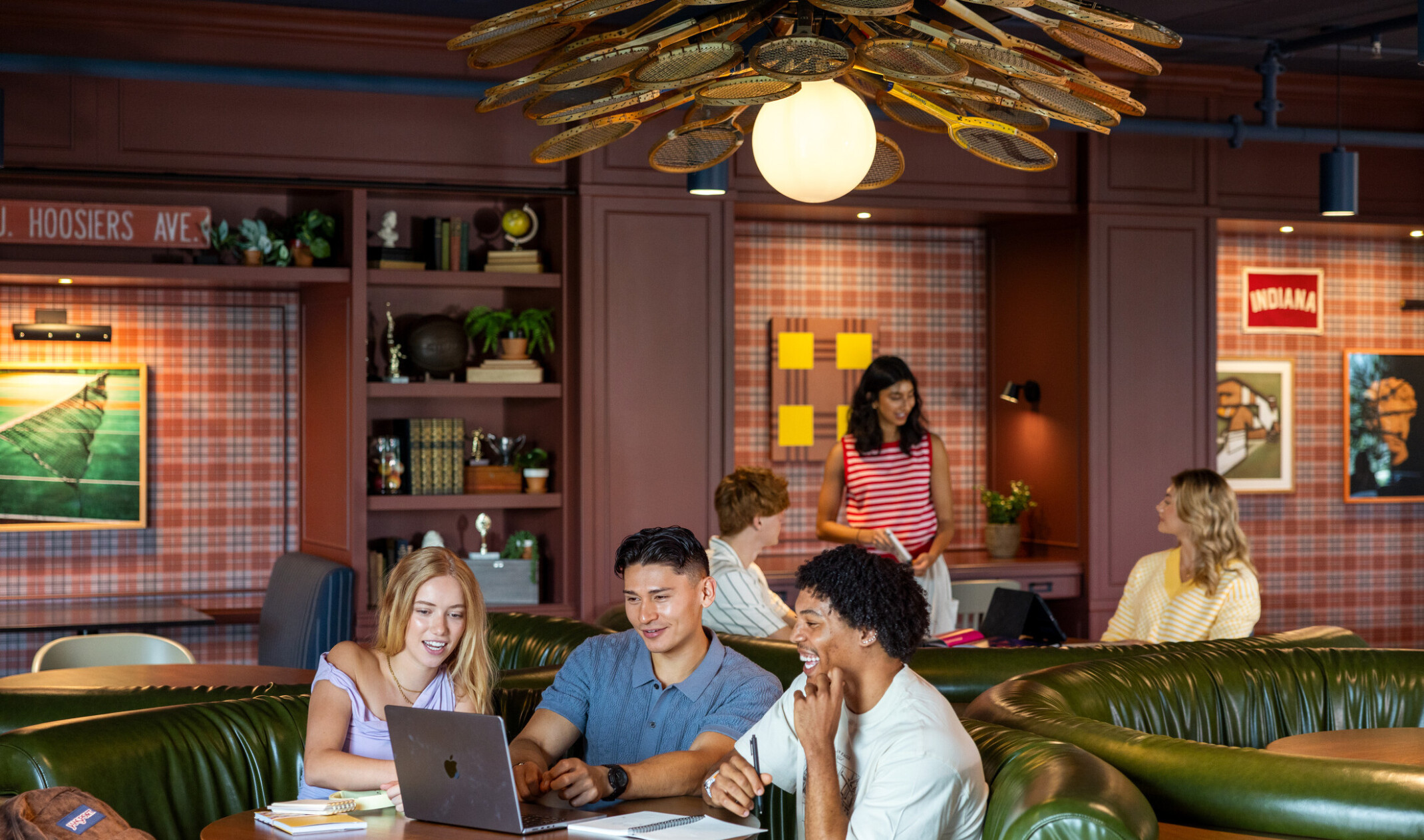 Hub Bloomington off campus student housing; Students studying and talking in booth seating under a badminton-racket light fixture.