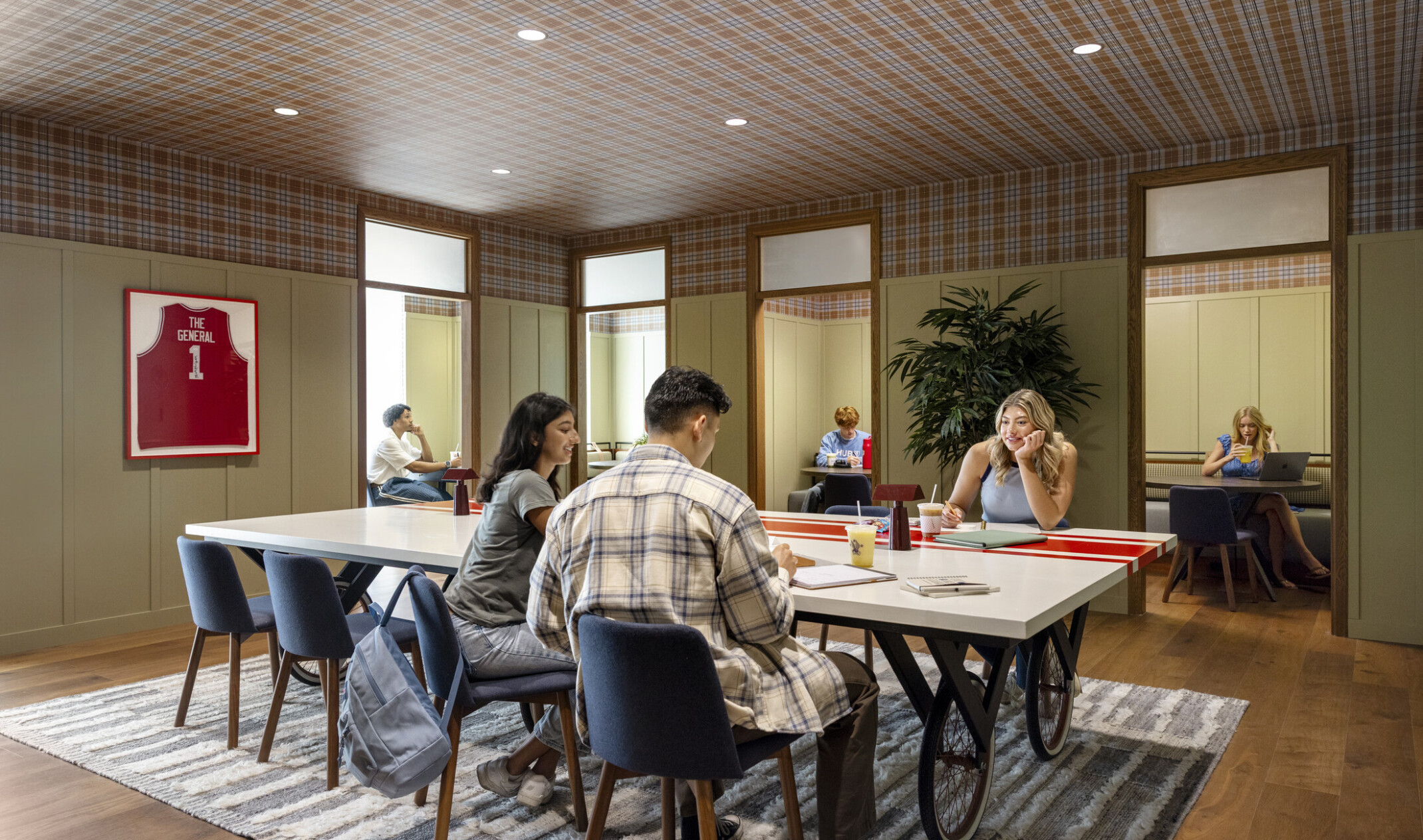 Hub Bloomington off campus student housing; Annex with plaid ceiling, bike-wheel table, and students studying.