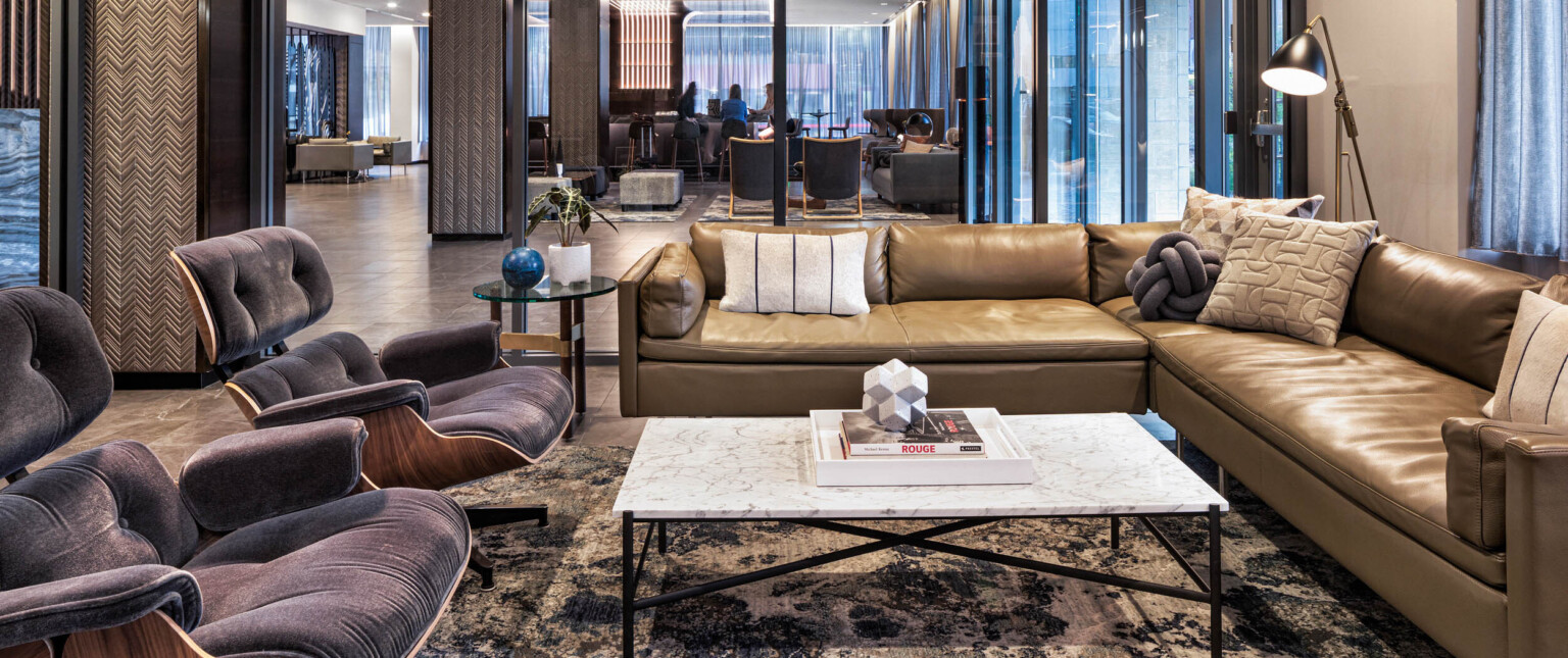 Seating area with couch and arm chairs around coffee table front, sectioned off by glass partition with full length windows following Marriott brand architecture