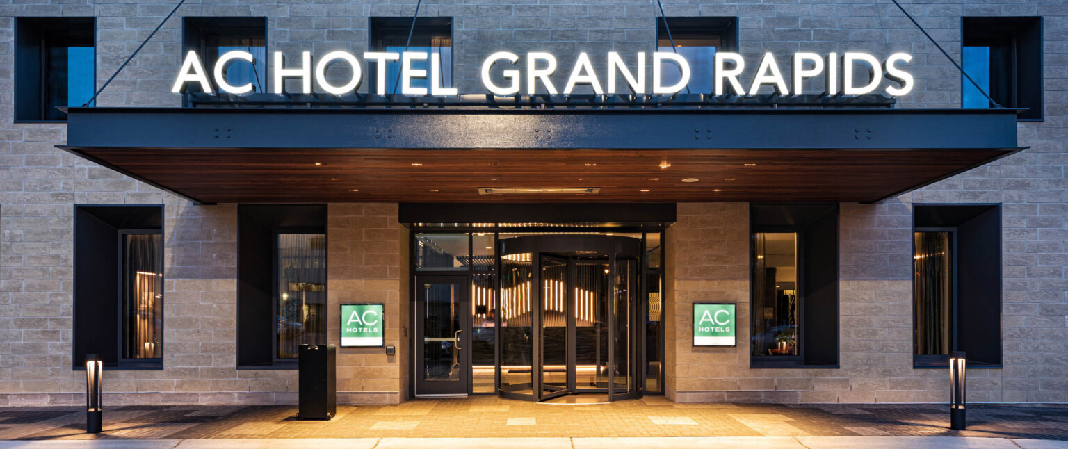 Close up of hotel entry with name illuminated above and signage on stone walls on either side of revolving door