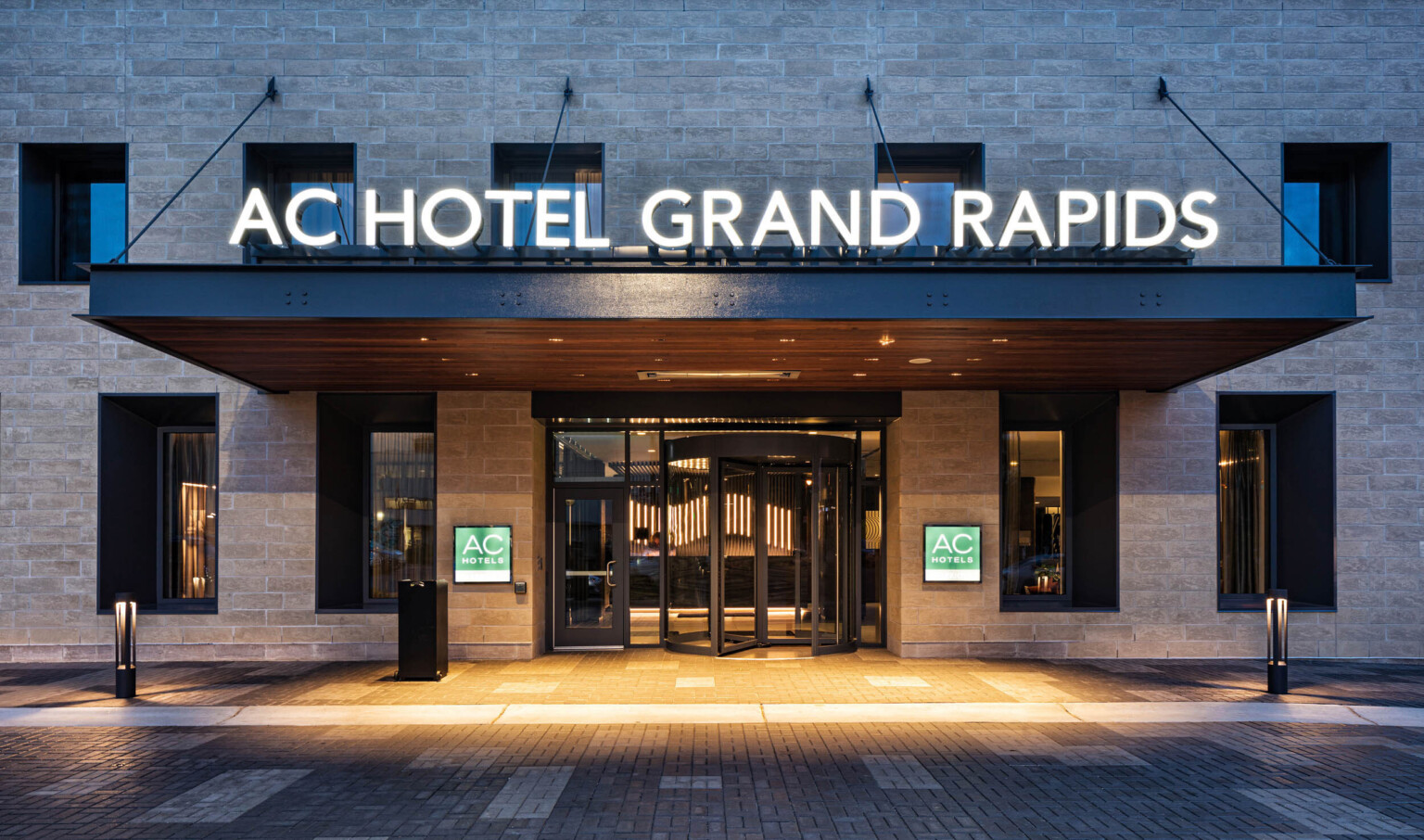 Close up of hotel entry with name illuminated above and signage on stone walls on either side of revolving door