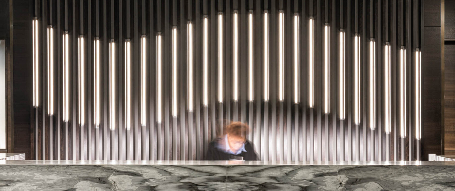 Dark marbled reception desk in lobby with thin pillared wall details, partially illuminated curve along center following Marriott brand architecture