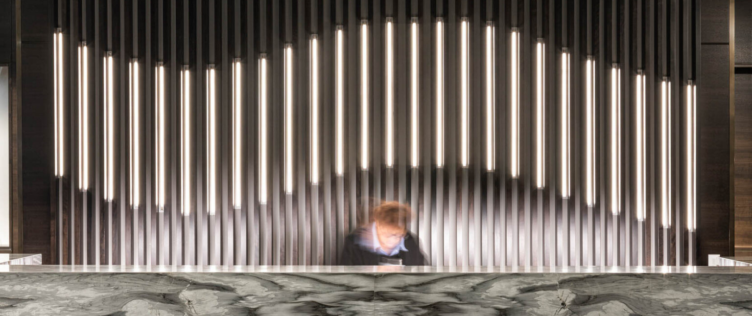 Dark marbled reception desk in lobby with thin pillared wall details, partially illuminated curve along center